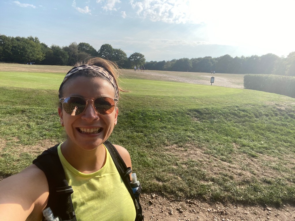 Image of a girl taking a selfie after a run in a yellow top and sunglasses, on a sunny day with green fields behind her