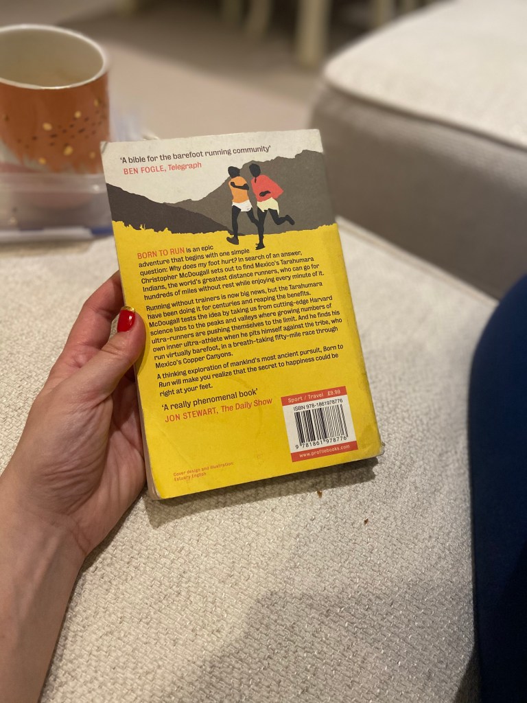 The back cover of the book Born to Run by Christopher McDougall held against a cream sofa with a pink mug in the background