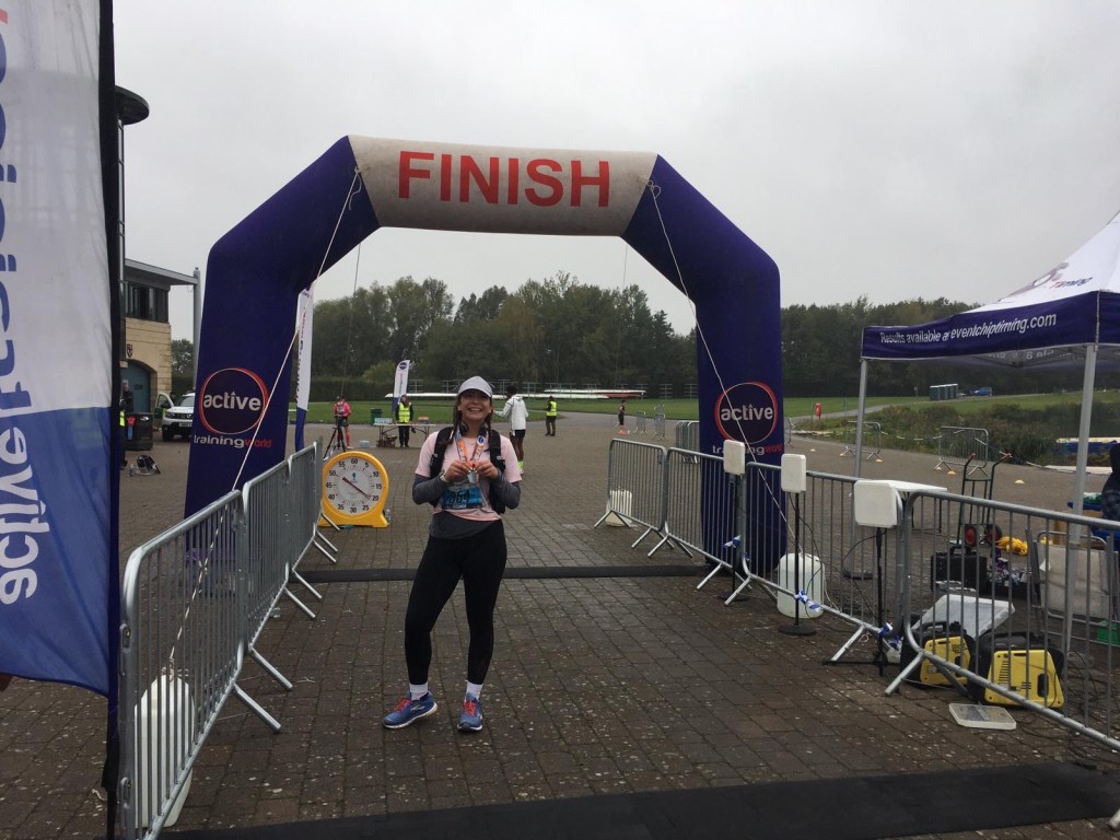 A woman wearing leggings, a tshirt and a cap holding a medal with an inflatable blue finish line behind her