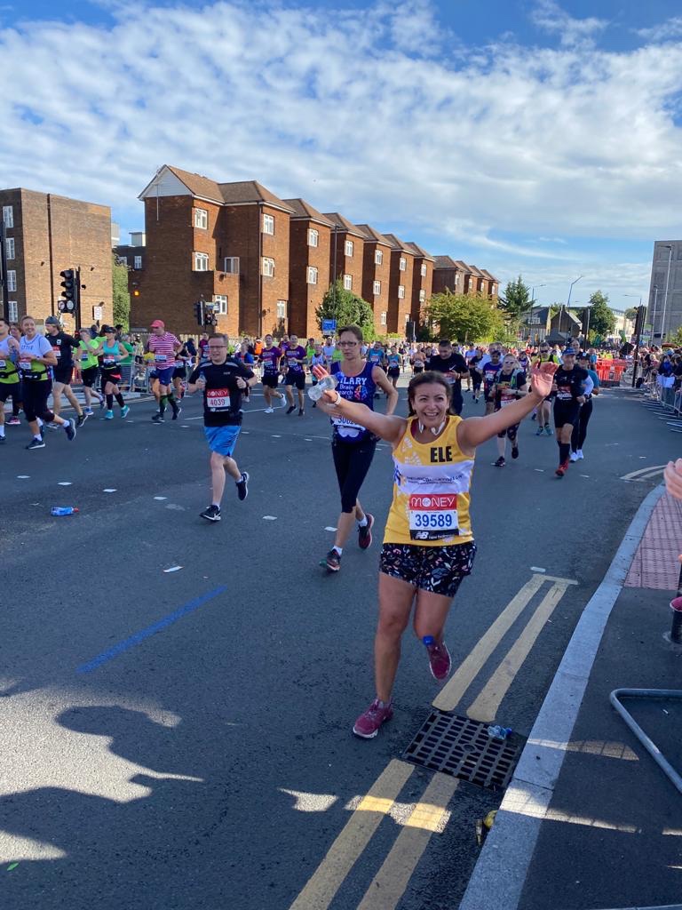 Woman running at the London Marathon wearing a yellow charity vest and colourful shorts 
