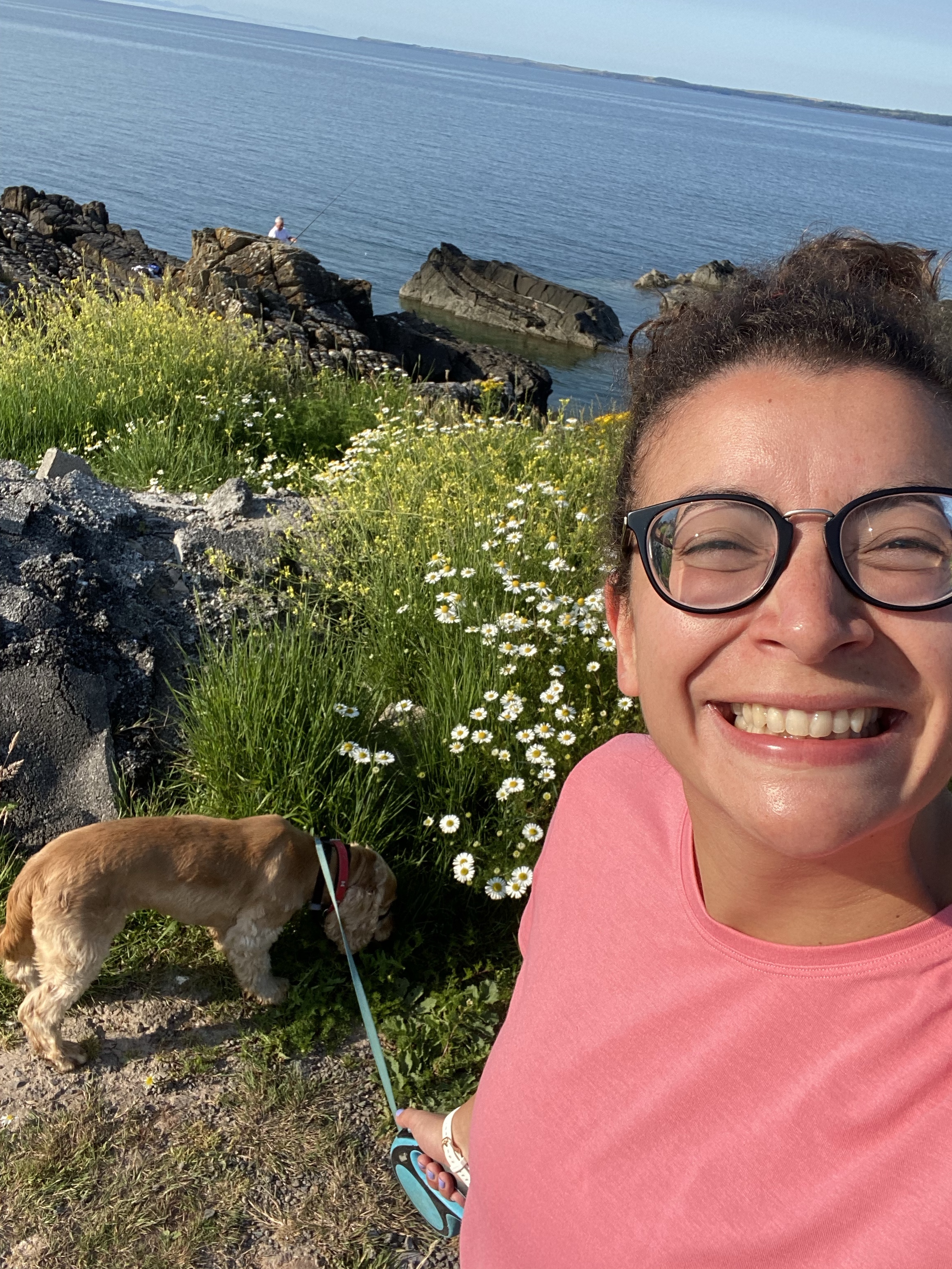 A selfie of a woman running by water holding a golden cocker spaniel dog on a blue lead