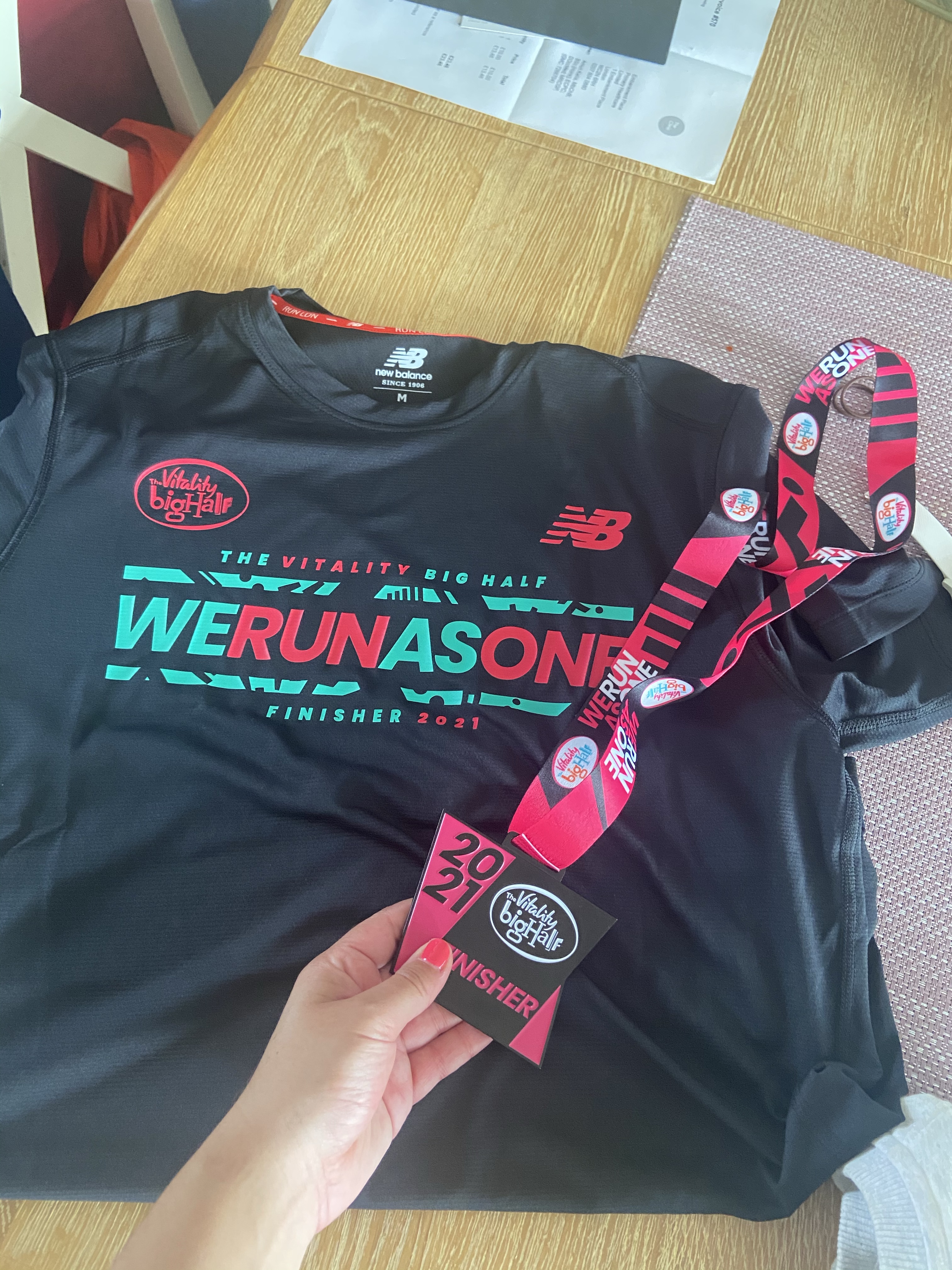 A black running t-shirt from the Vitality Big Half reading 'We Run as One' next to a pink and black metal medal