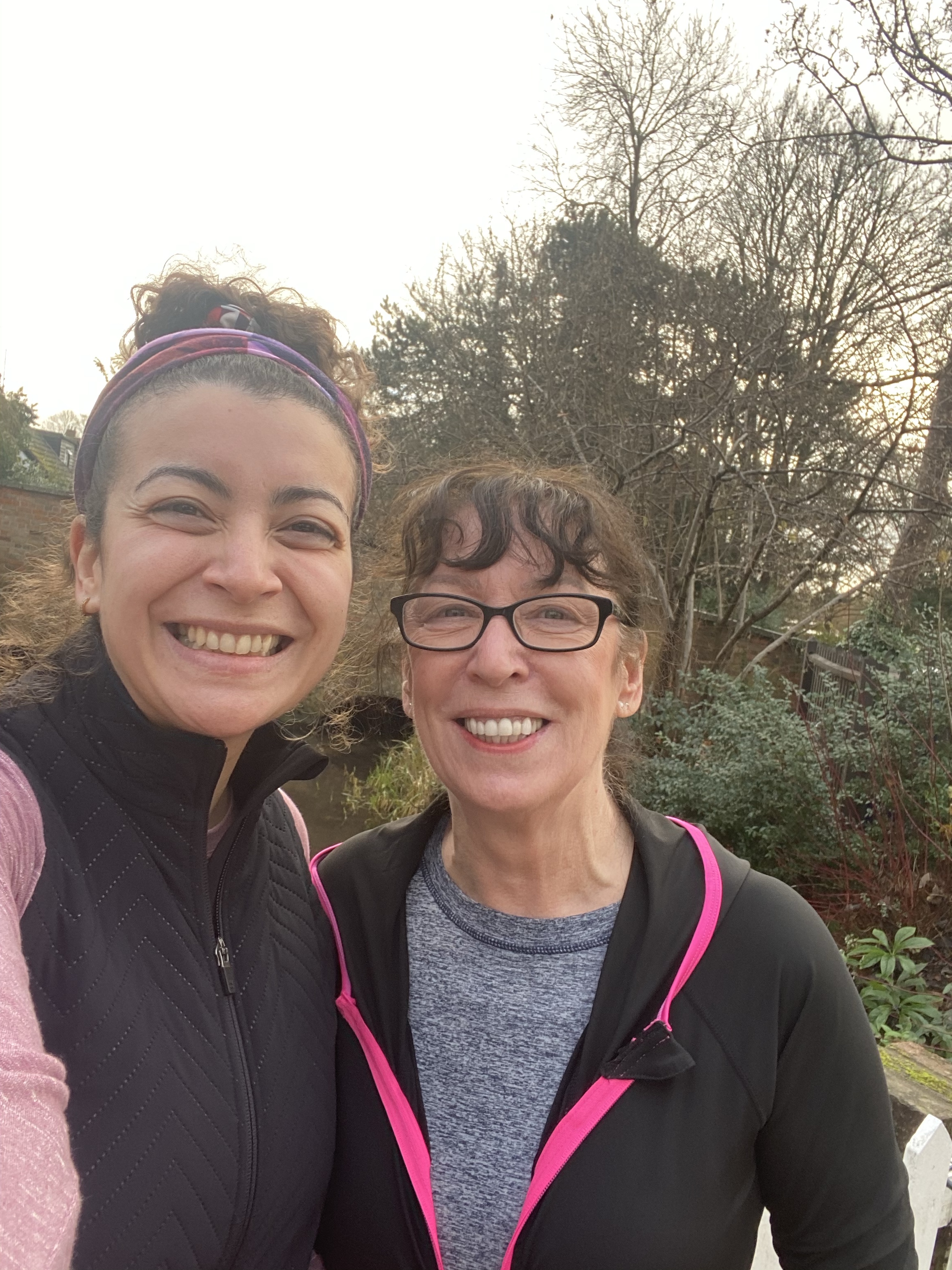 Two women smiling at the camera wearing black and pink running clothes with trees behind them