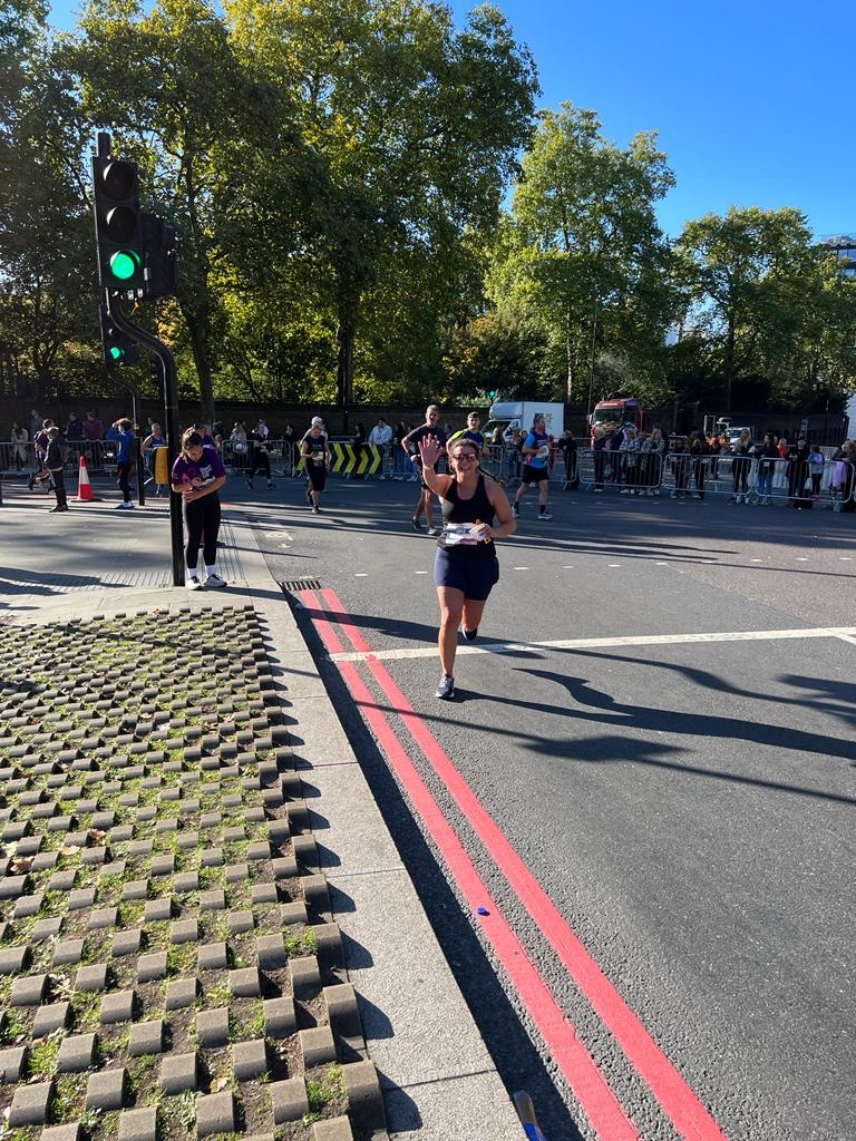 Woman running on the road and waving to the camera at the Royal Parks Half Marathon in London