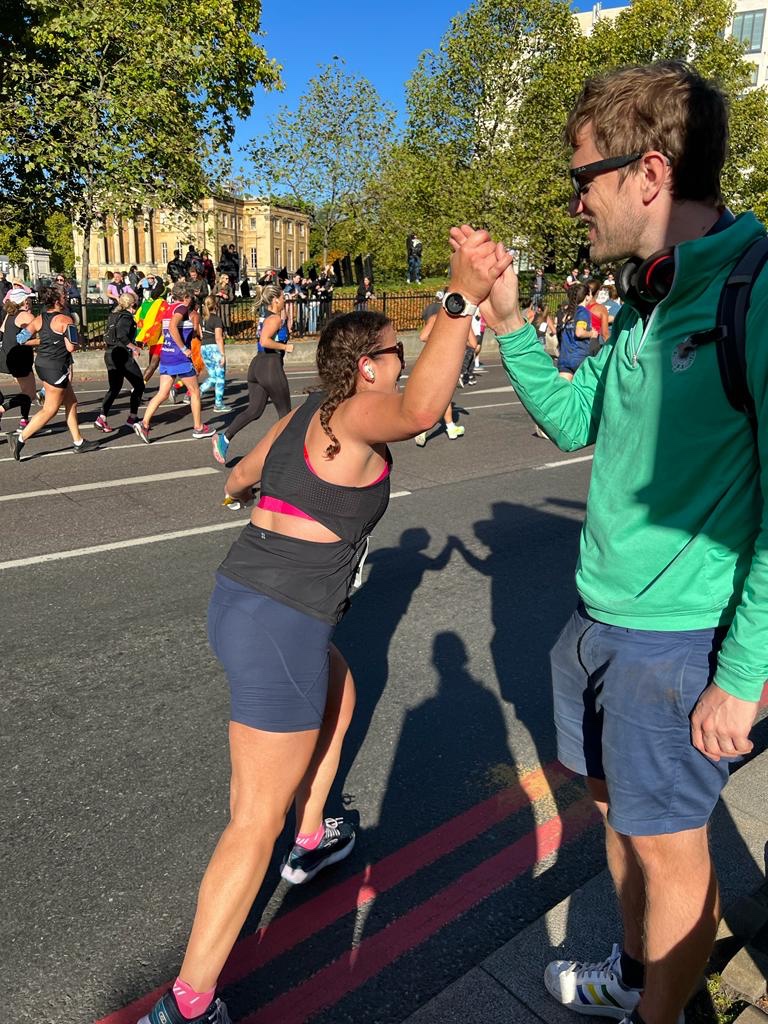 Woman running along the road at the Royal Parks Half Marathon high-fiving a supporter in the crowd
