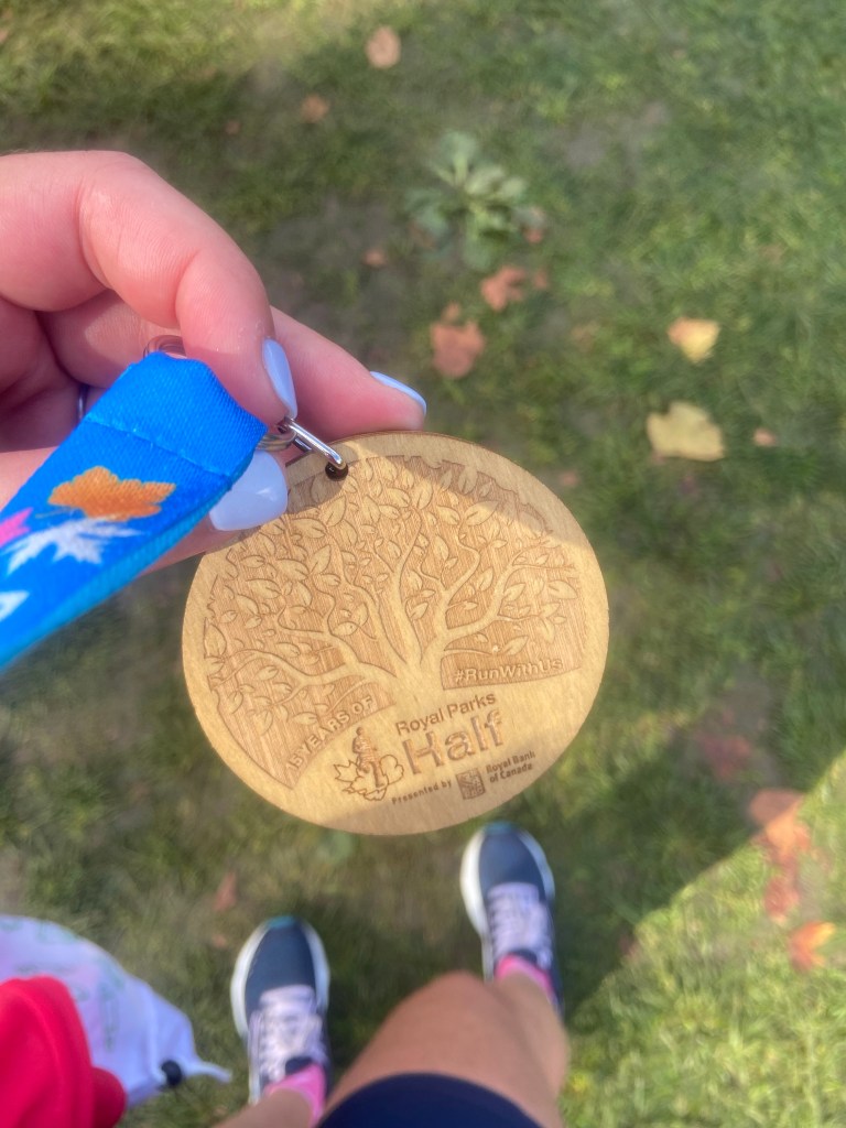 A wooden meal with a blue lanyard from the Royal Parks Half Marathon, with a backdrop of green grass