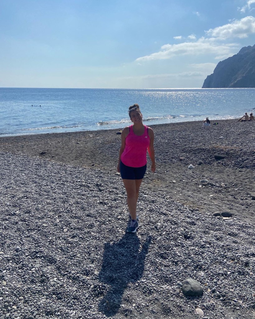 Girl wearing shorts and a pink vest top standing on a beach in Santorini, Greece