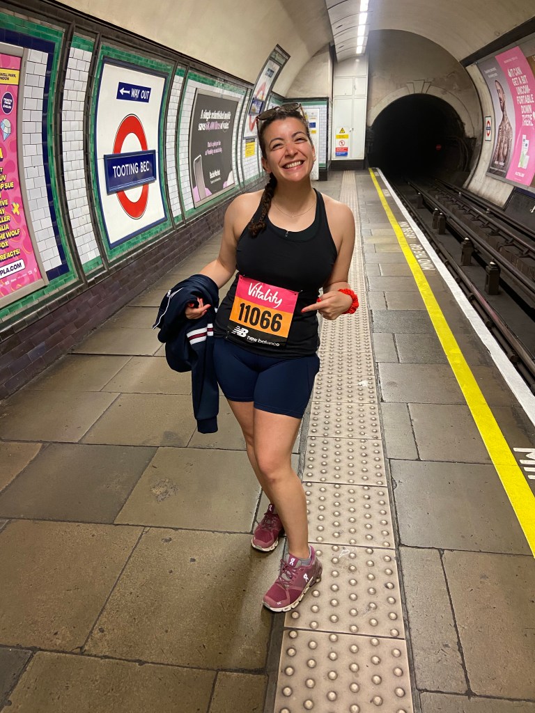 A woman standing at Tooting Bec London Underground tube platform wearing running clothes on the way to a Vitality race