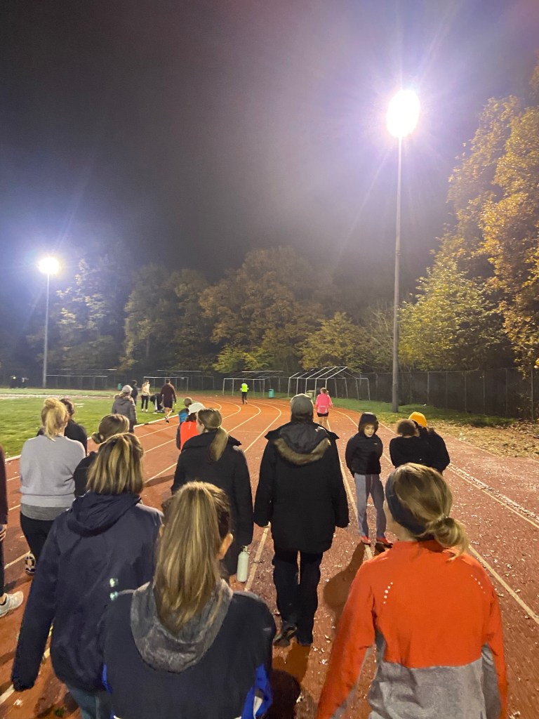 A group of people walking along Tooting Bec athletics running track in the evening