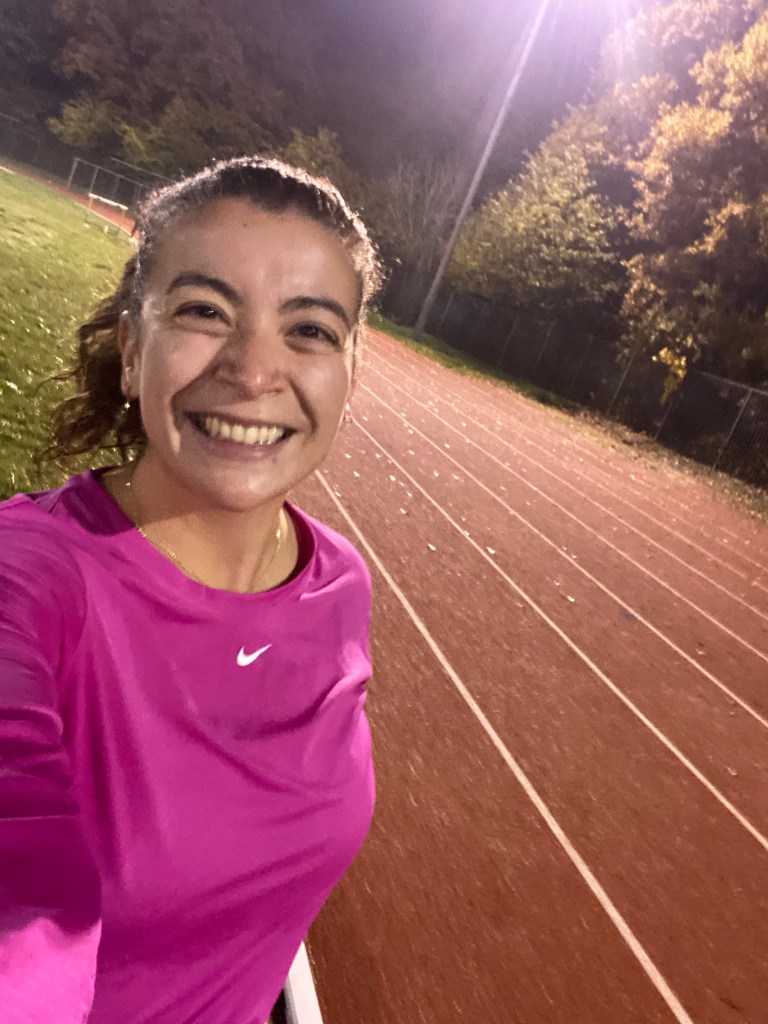 A girl with brown hair standing next to the Tooting Athletics Track in the evening
