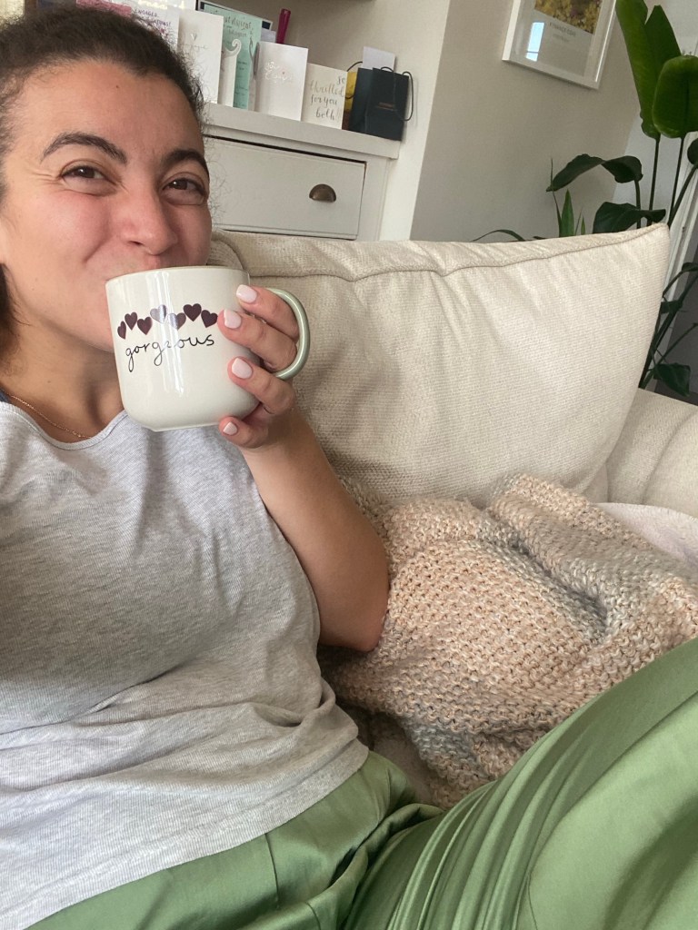 Image of a girl in pyjamas sitting on a cream sofa drinking a cup of tea